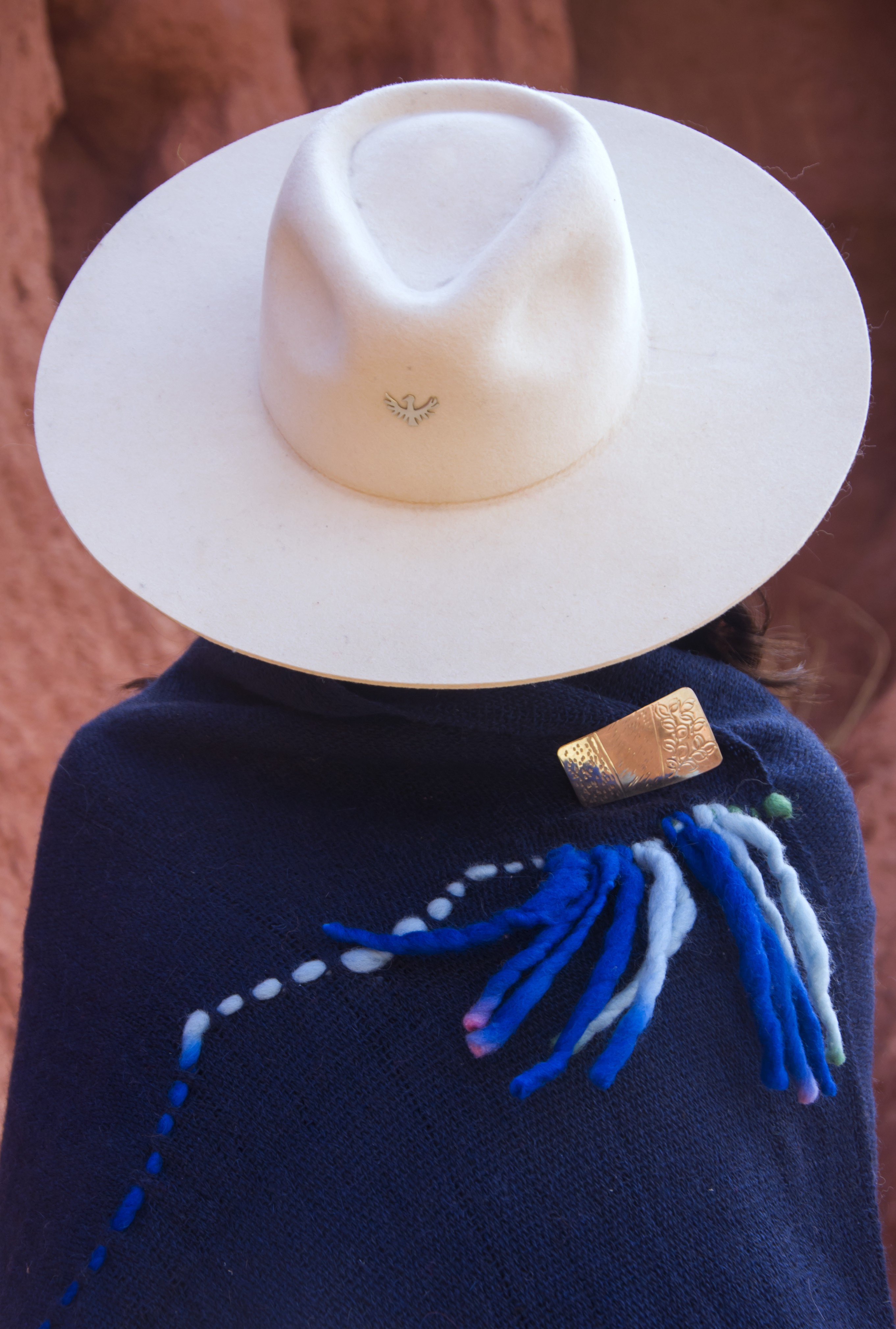Sombrero de fieltro blanco y prendedor de alpaca cincelado a mano, sobre manta de fibra de llama